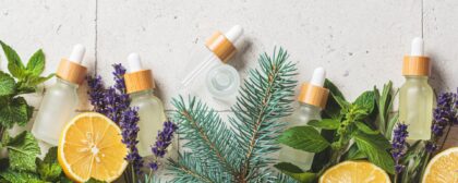 Essential oils of lavender, spruce, lemon, and mint in glass bottles, amongst fresh ingredients.