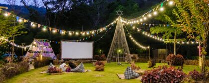 Outdoor cinema in a thriving garden with fairy lights, a big screen, and comfortable seating.