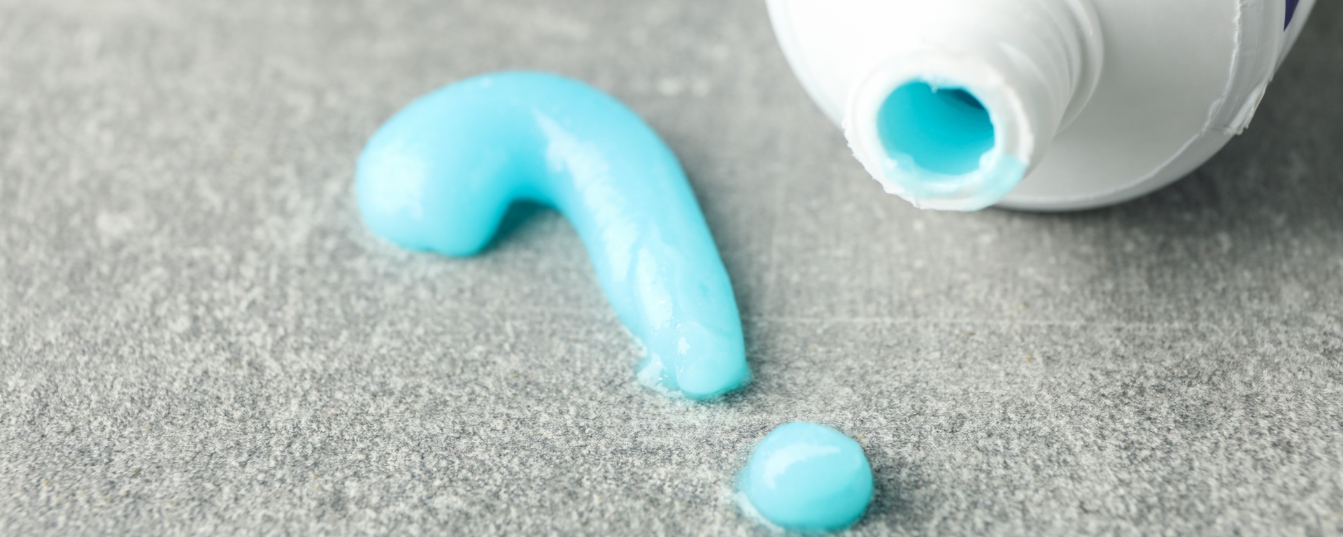 Close-up of question mark made of toothpaste and tube on grey background.