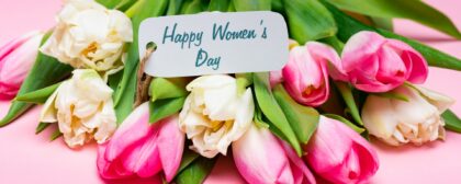 Flowers on a pink background with a 'Happy Women's Day' card attached to them