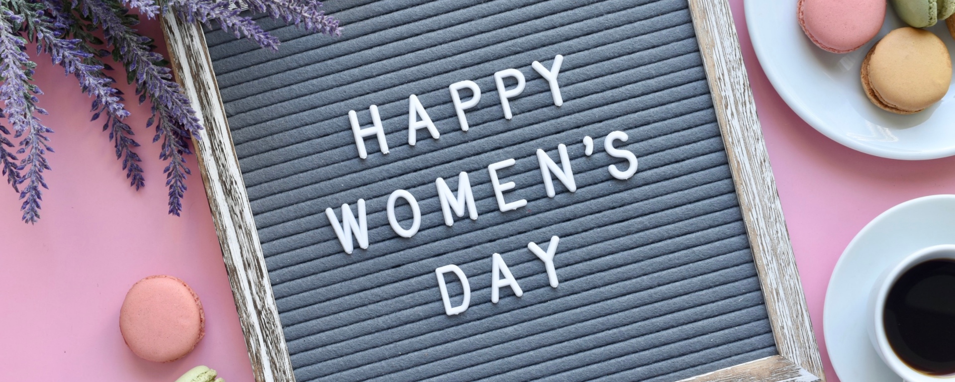 "Happy Women's Day" message on a little black board on a pink background, with macaroons next to it.